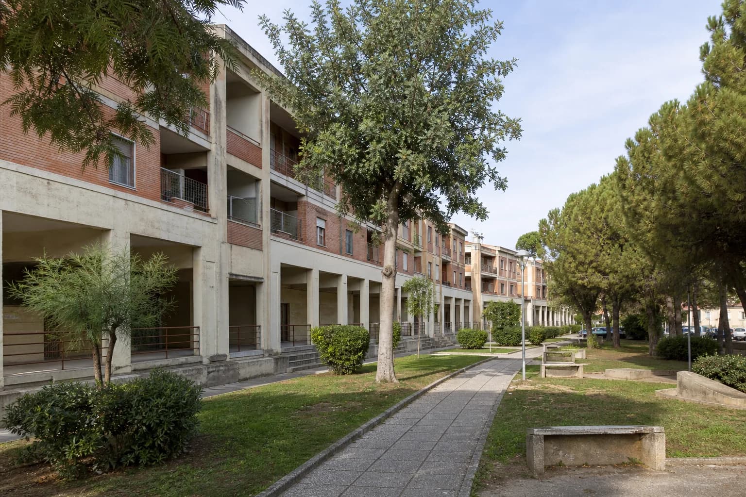 Brick and concrete apartment blocks facing a green pedestrian space in Matera’s Spine Bianche district